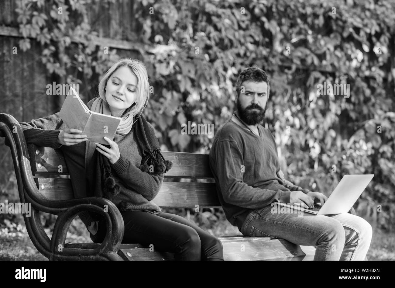 books against computers. booklover in park. bearded man and woman on bench in park. spring weekend relax. first meet of smart couple. students life. woman read book. man use computer technology. Stock Photo