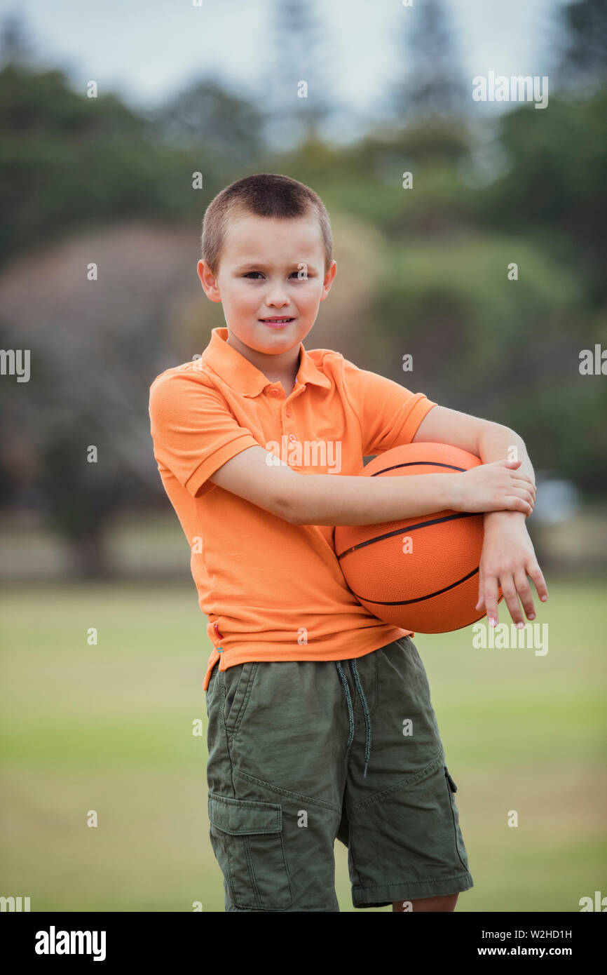 A portrait shot of a young caucasian boy wearing casual clothing, he is holding a basketball and looking at the camera. Stock Photo