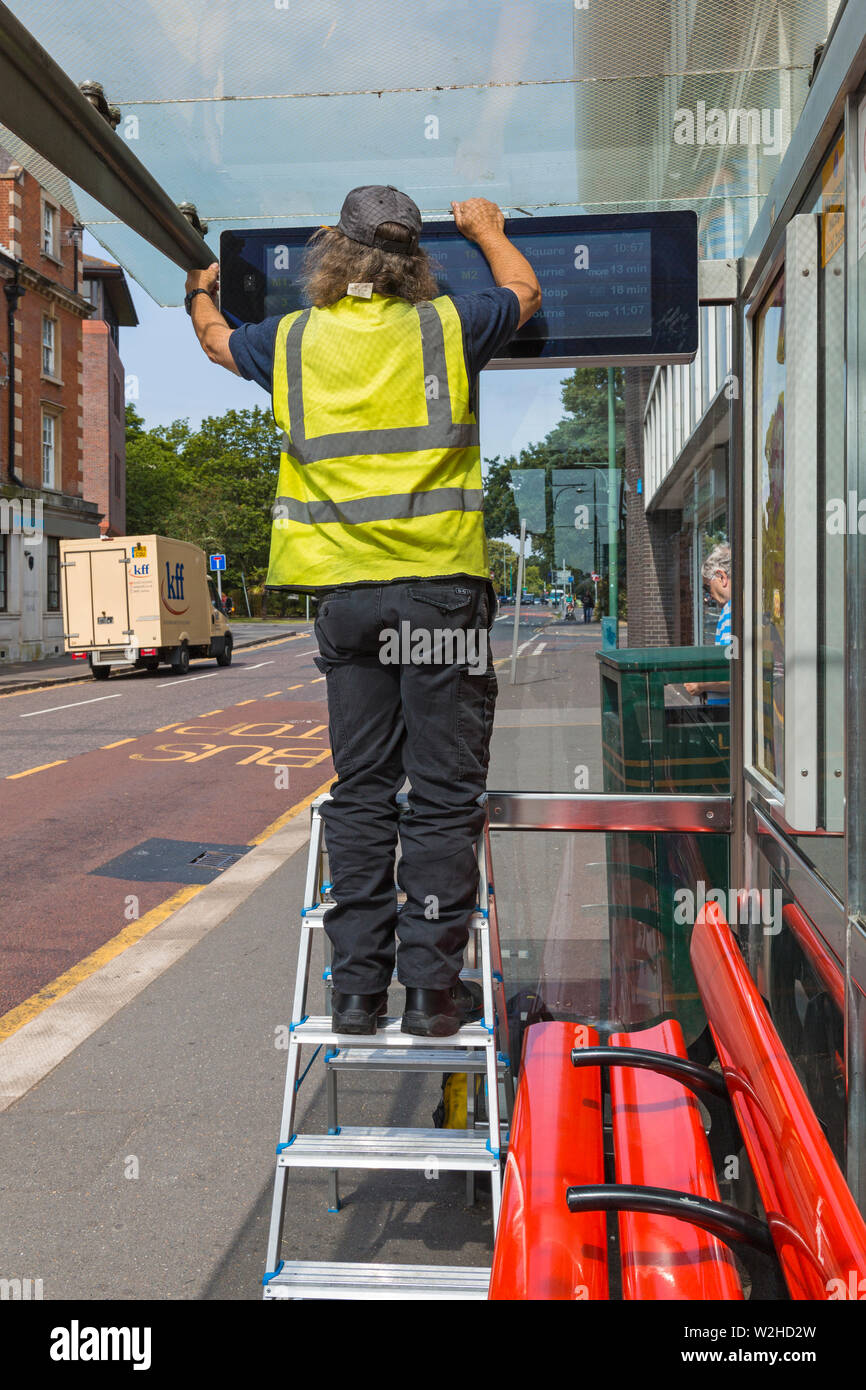 Engineer checking, repairing, RTPI display sign, real time passenger information, electronic digital data sign, at bus stop shelter in Bournemouth Stock Photo