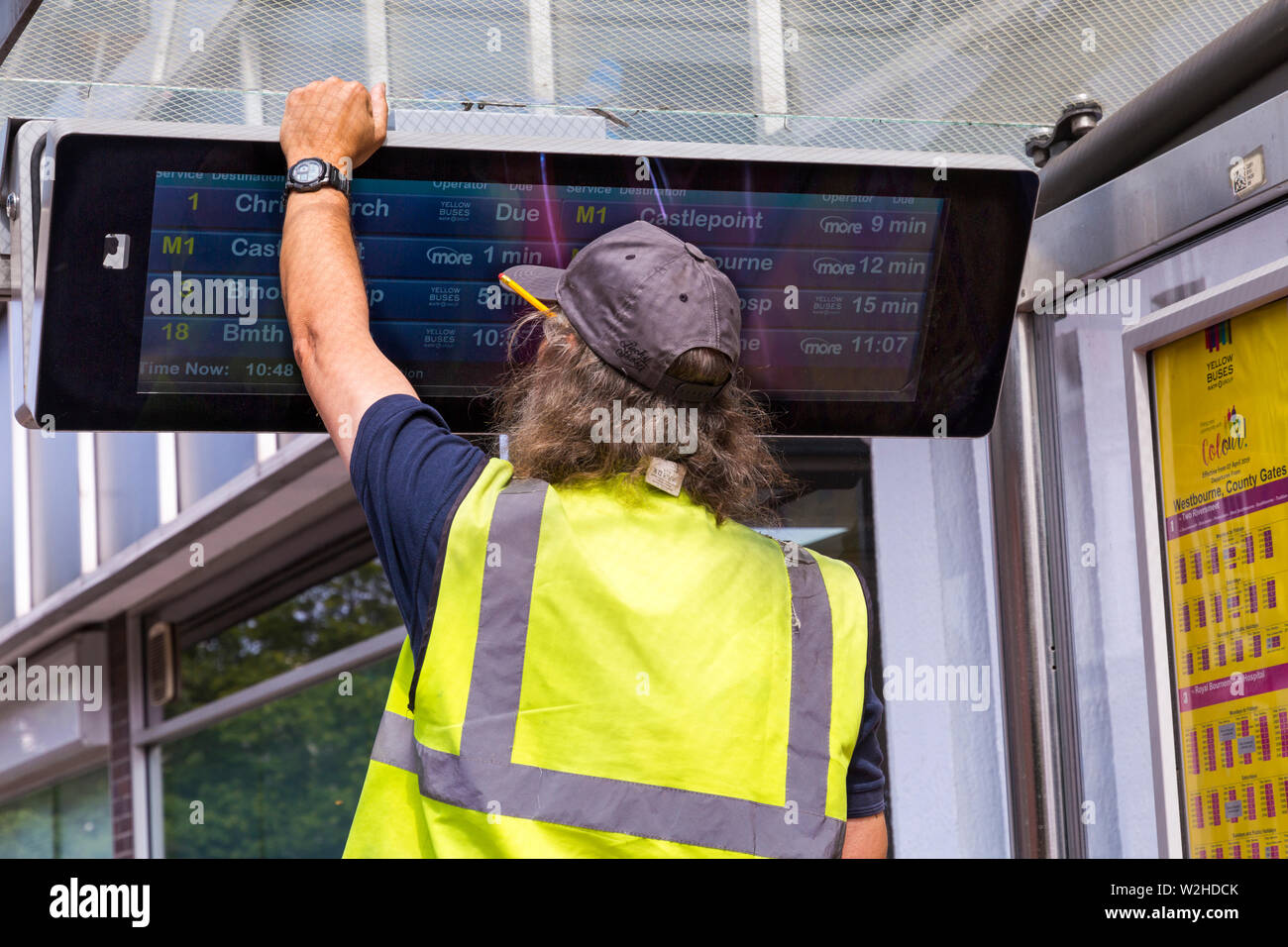 Engineer checking, repairing, RTPI display sign, real time passenger information, electronic digital data sign, at bus stop shelter in Bournemouth Stock Photo