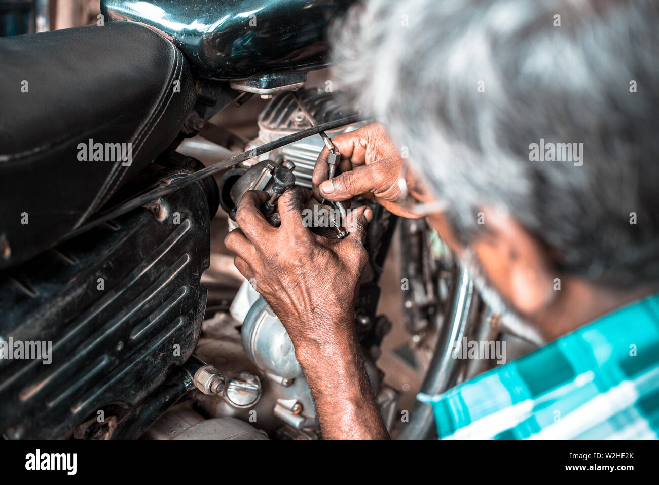 A mechanic in a small workshop in India, repairing the carburettor on an old motorcycle. Stock Photo