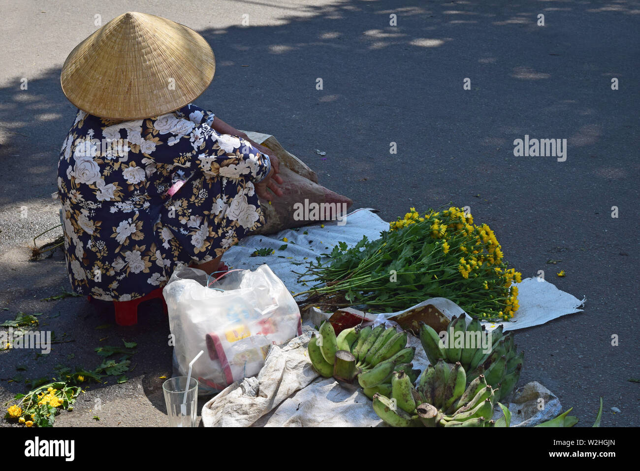Hanoi, Vietnam, April 3, 2019: A vietnamese woman seated on the road sells yellow flowers. Woman Vendor of flowers on the street of Ha Noi, Vietnam. Stock Photo
