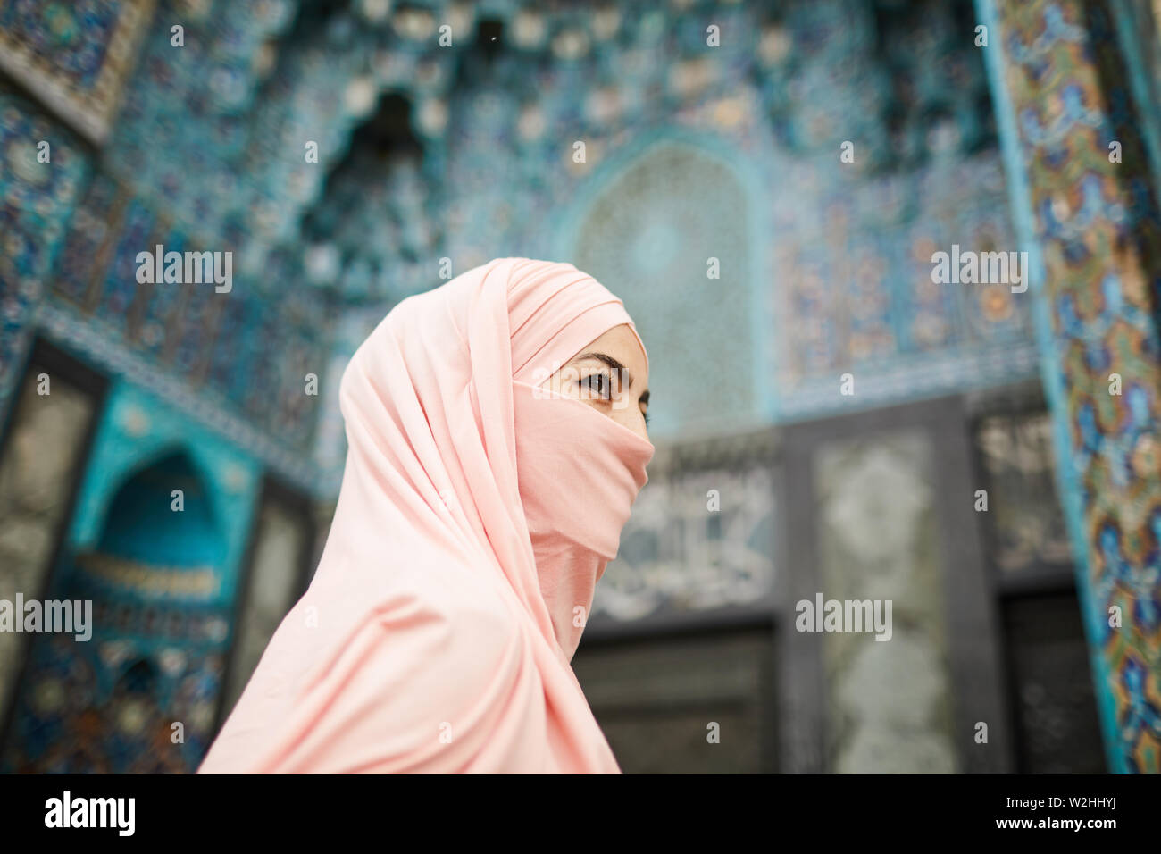 Enigmatic Muslim lady with covered face going to beautiful mosque with ornamental design and looking away Stock Photo