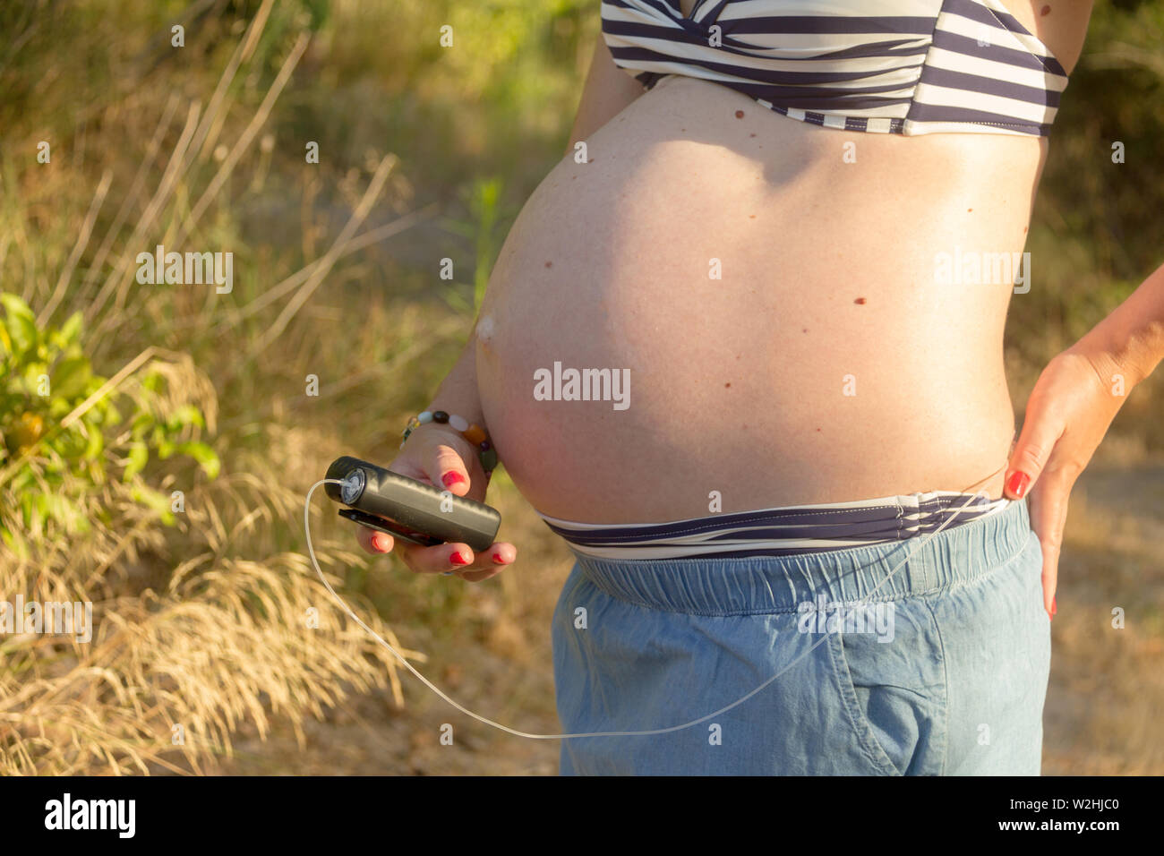 A diabetic pregnant woman with an insulin pump in a forest. She's wearing a blue skirt and a