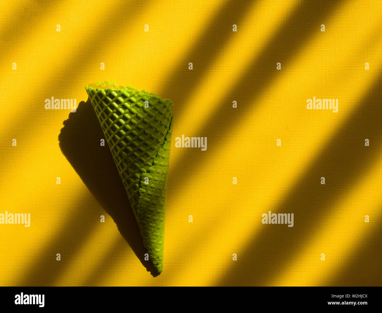 Green ice cream cone on yellow background with shadows Stock Photo - Alamy