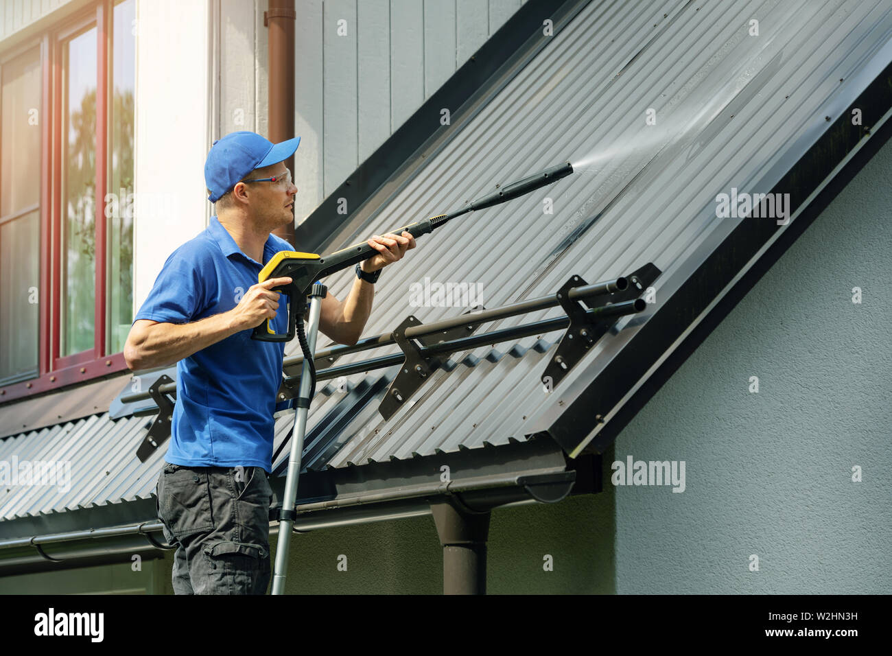 man standing on ladder and cleaning house metal roof with high pressure washer Stock Photo