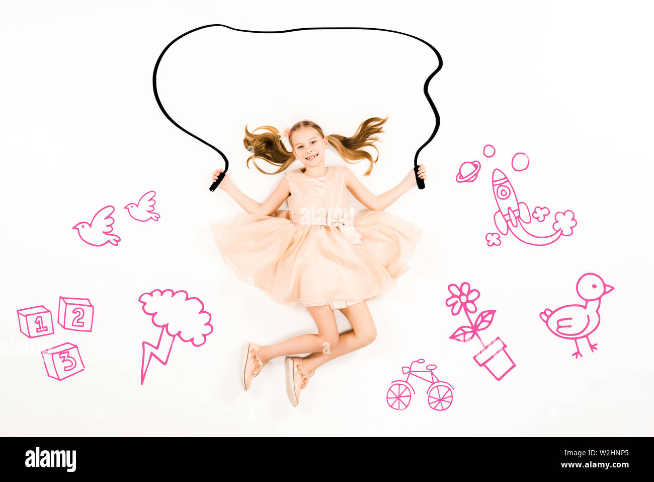 top view of cheerful kid flying with jumping rope and smiling on white ...