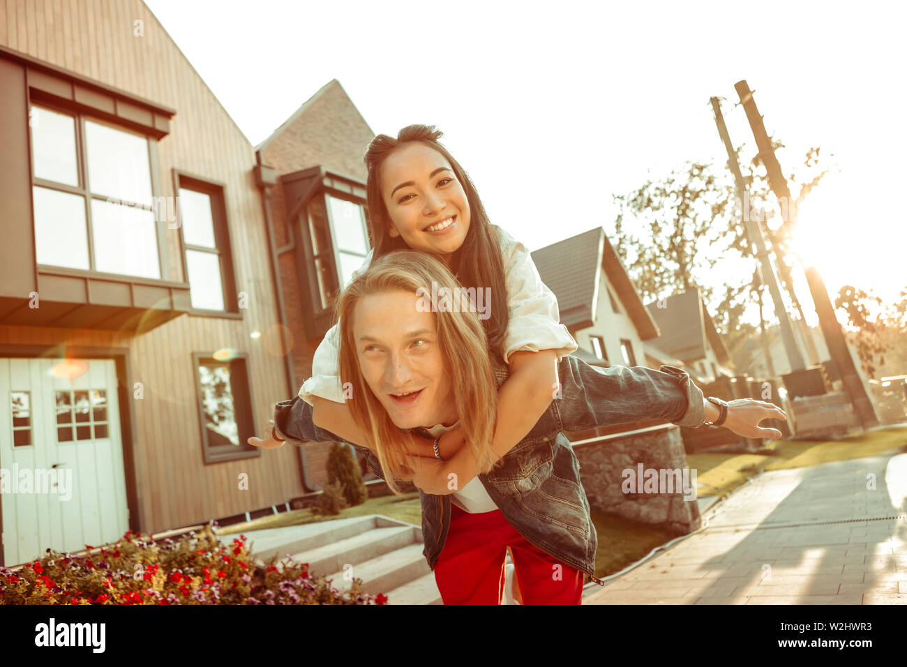 Beaming dark-haired girl tightly hugging her long-haired boyfriend Stock Photo