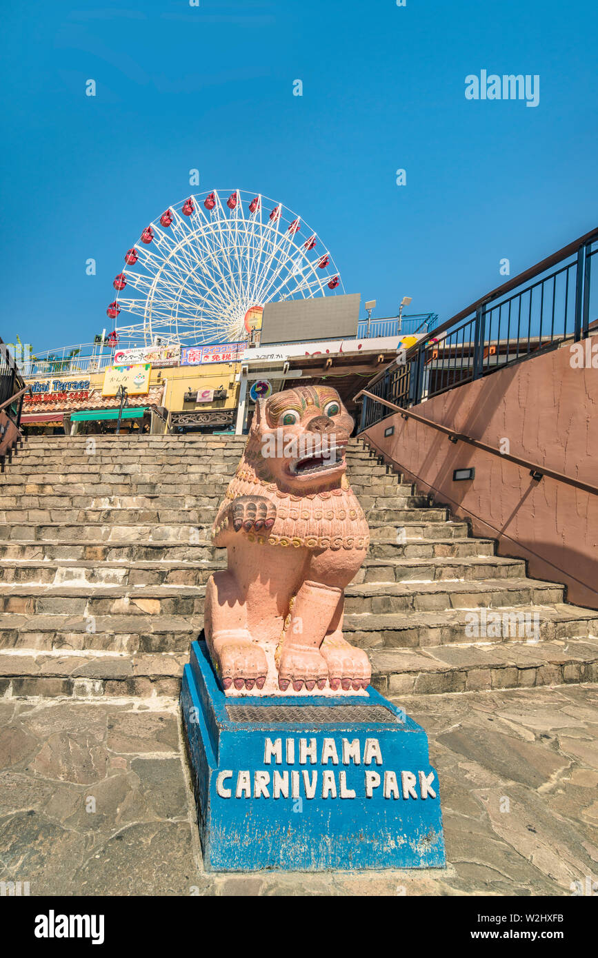 Okinawan Shisa lion and Mihama Carnival Park Ferris wheel located in the American Village neighborhood of Chatan City decorated with palm trees near S Stock Photo