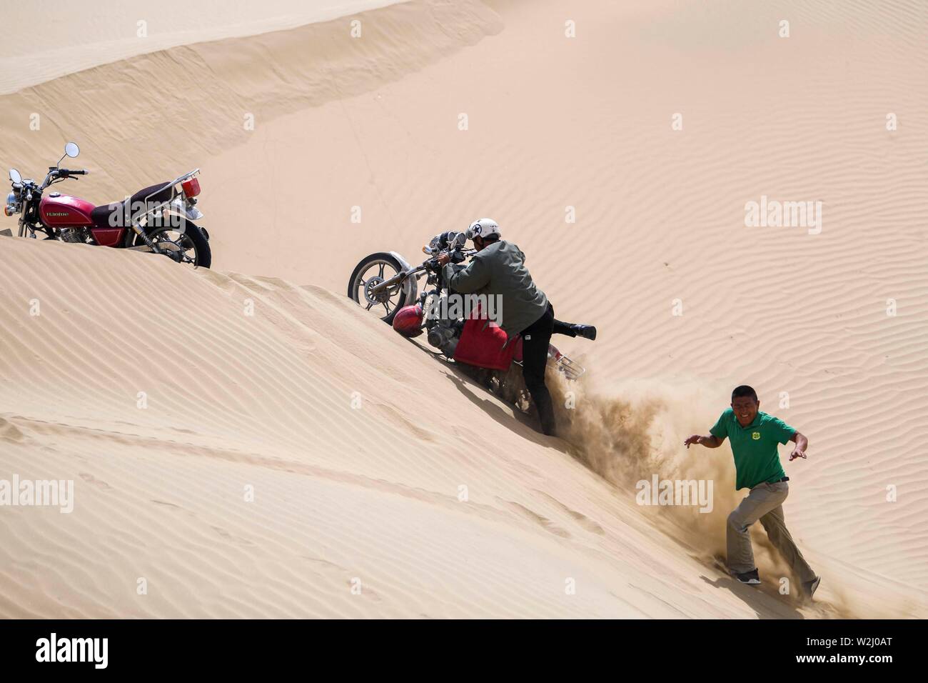 (190709) -- YULI, July 9, 2019 (Xinhua) -- Forest rangers try to pull a motorcycle out of sand on their patrol way in Yuli County, northwest China's Xinjiang Uygur Autonomous Region, June 20, 2019. Wriggling along the rim of the Taklimakan desert, the 1,321-km-long Tarim River in northwest China's Xinjiang Uygur Autonomous Region nurtures the largest area of populus euphratica forests in the world.   As local government launched a project on populus euphratica forest restoration along the Tarim River three years ago, the vegetation has been increasing and forest rangers have been playing a mor Stock Photo