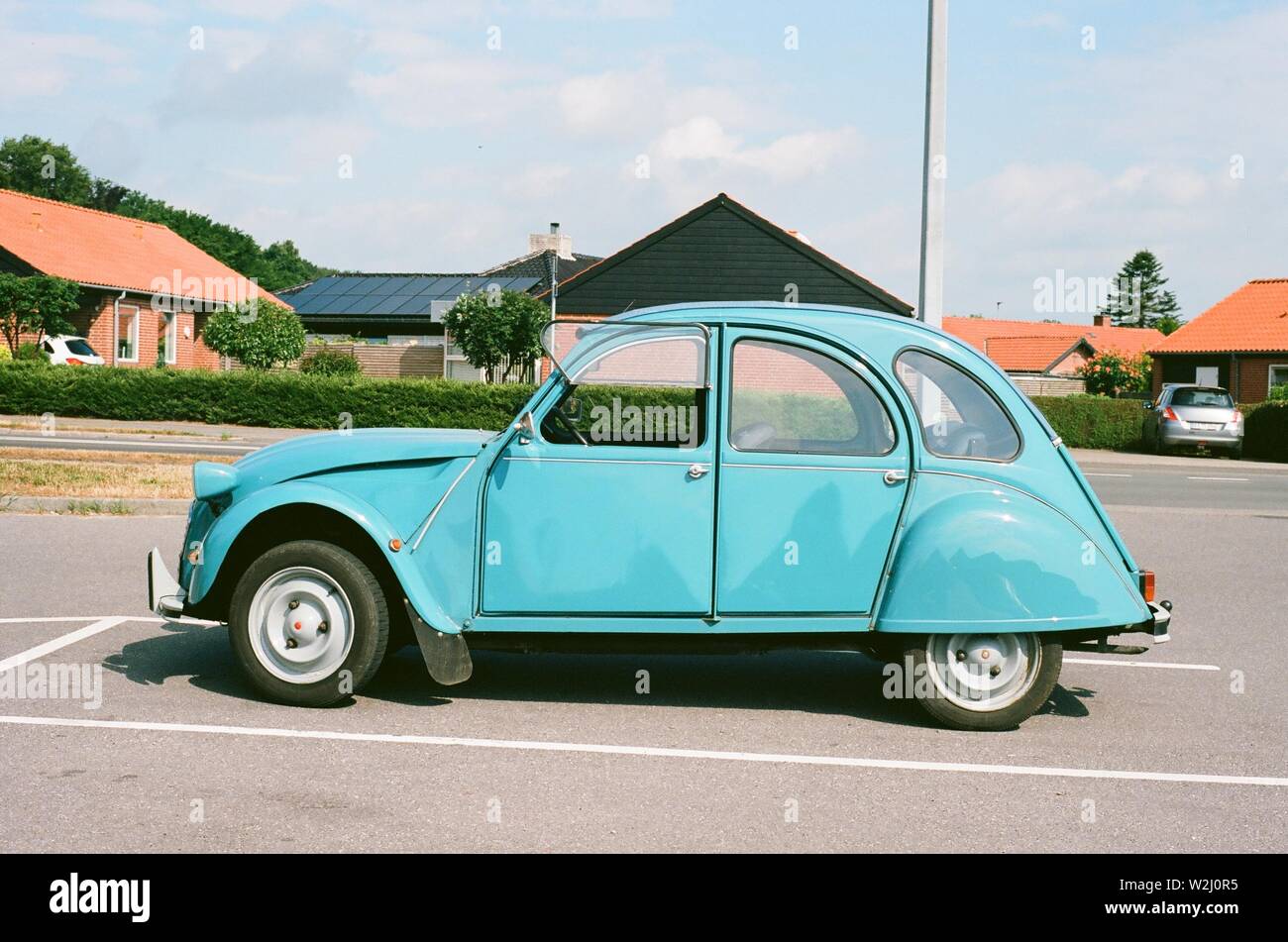 Blue Citroen Vintage car in a bright, sunny, parking lot. Summer in Denmark with cottages in background. Stock Photo