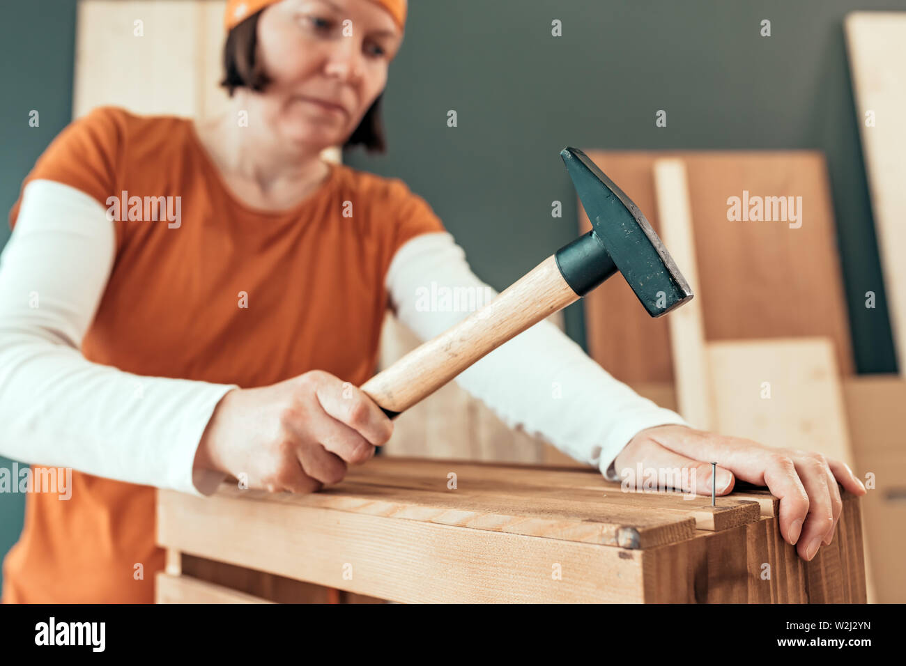 Female carpenter hammering nail into wooden crate in small business woodwork workshop, selective focus Stock Photo