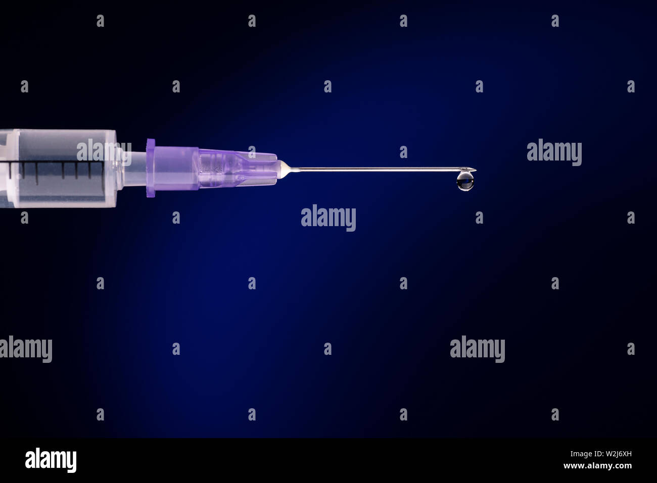Close-up of a syringe with cannula and drop in front of dark blue background Stock Photo