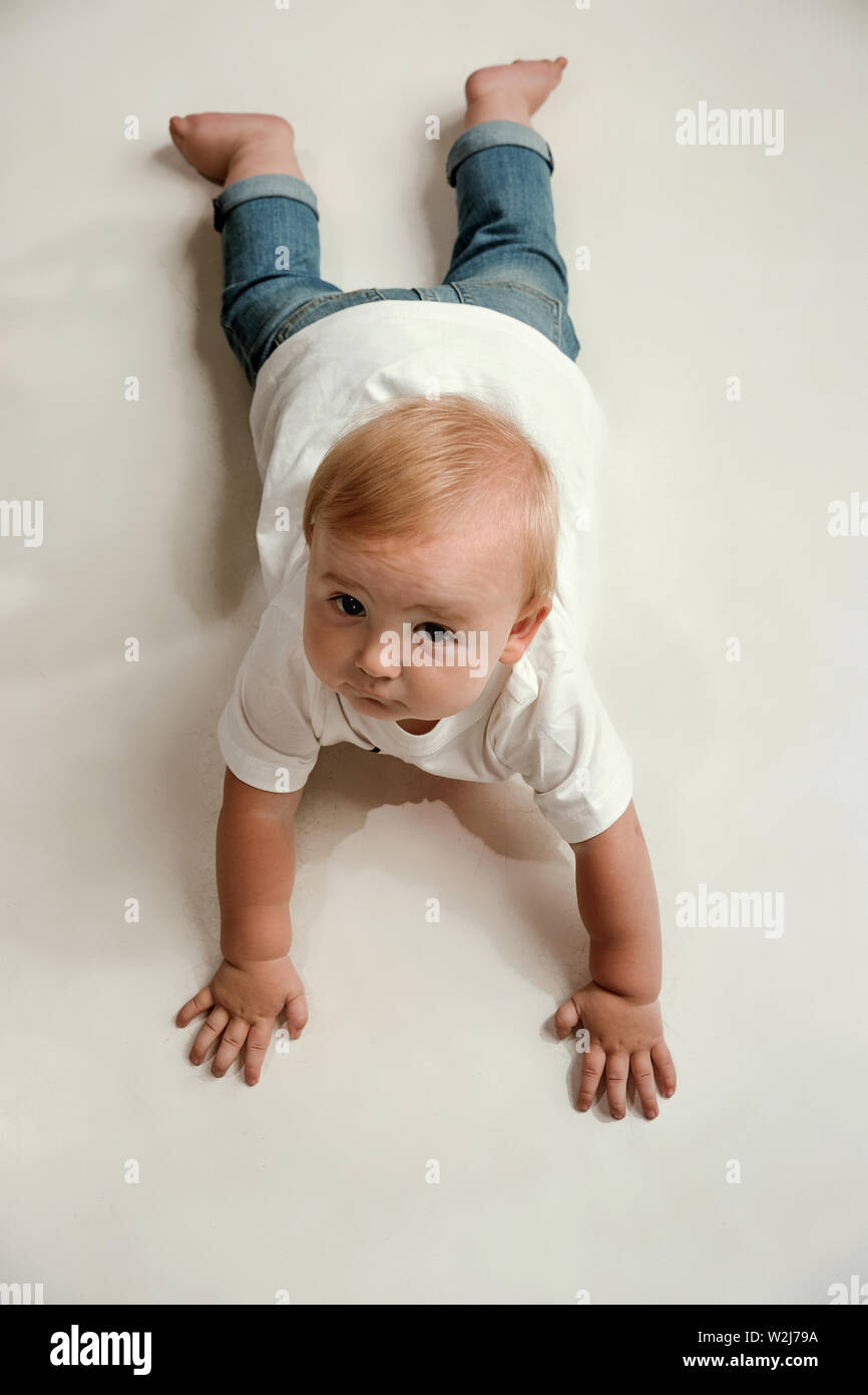 Little boy lying down on floor and looking up to the side. Cute child with big eyes in jeans and white shirt looks interested and dreaming. Concept of kid's rights, childhood, family lifestyle. Stock Photo