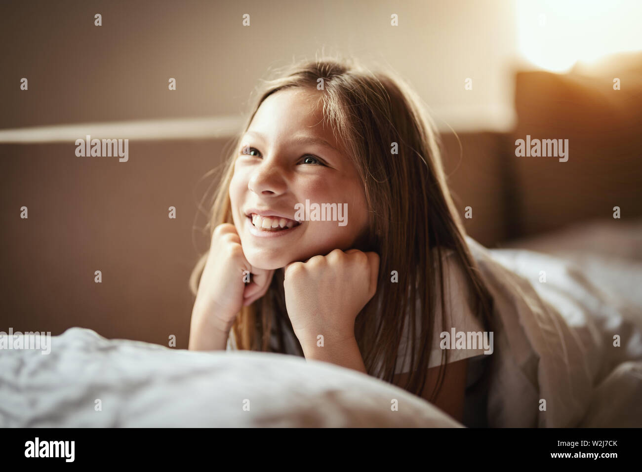 A happy little girl lies on the bed in the morning and laughs after awakening. Stock Photo