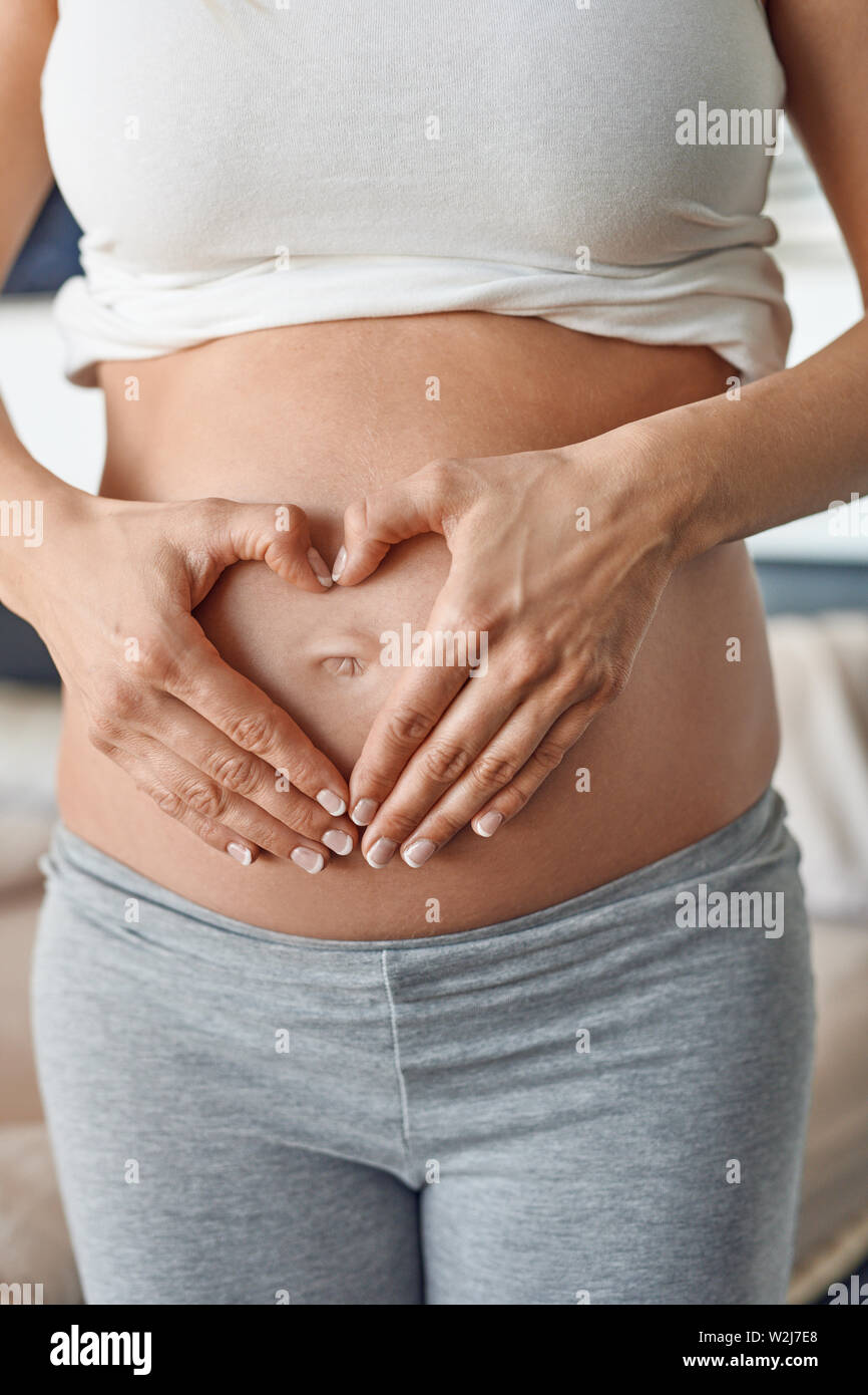 Young pregnant woman making a heart gesture with her hands around her bare belly button signalling her love for her unborn child Stock Photo