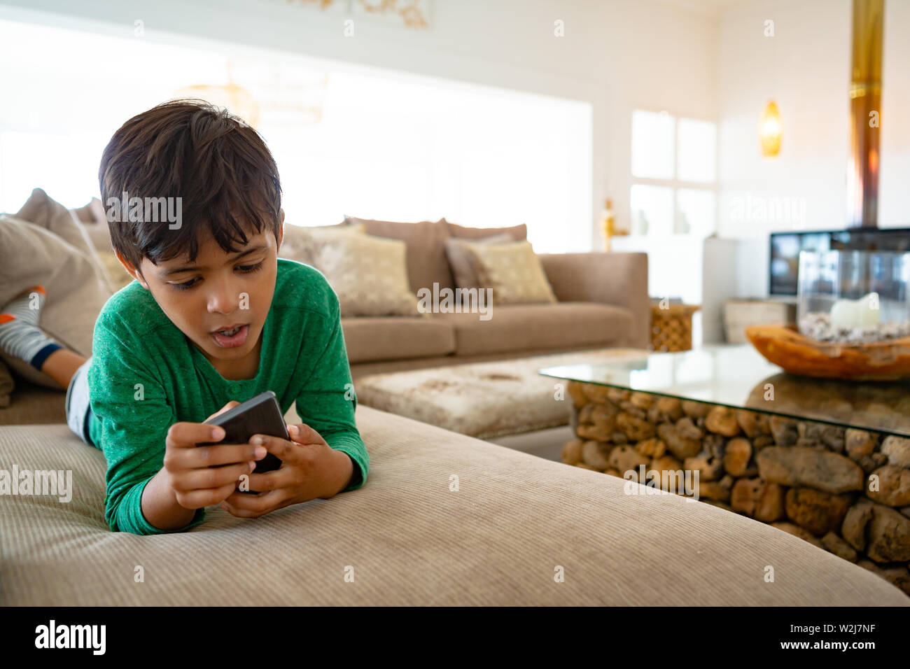 Boy using mobile phone while lying on sofa at home Stock Photo