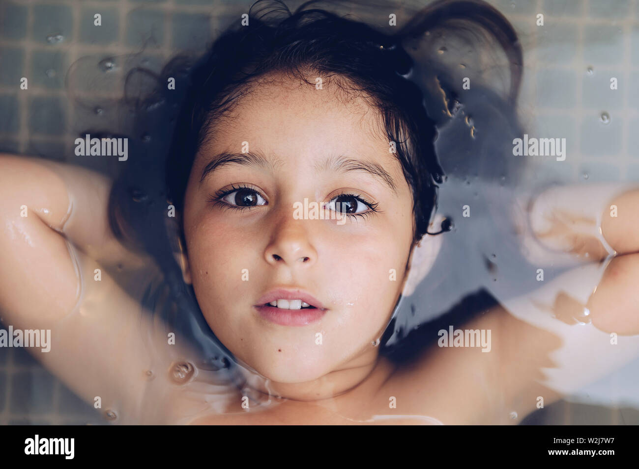 portrait of a happy beautiful little girl lying in the tub while taking