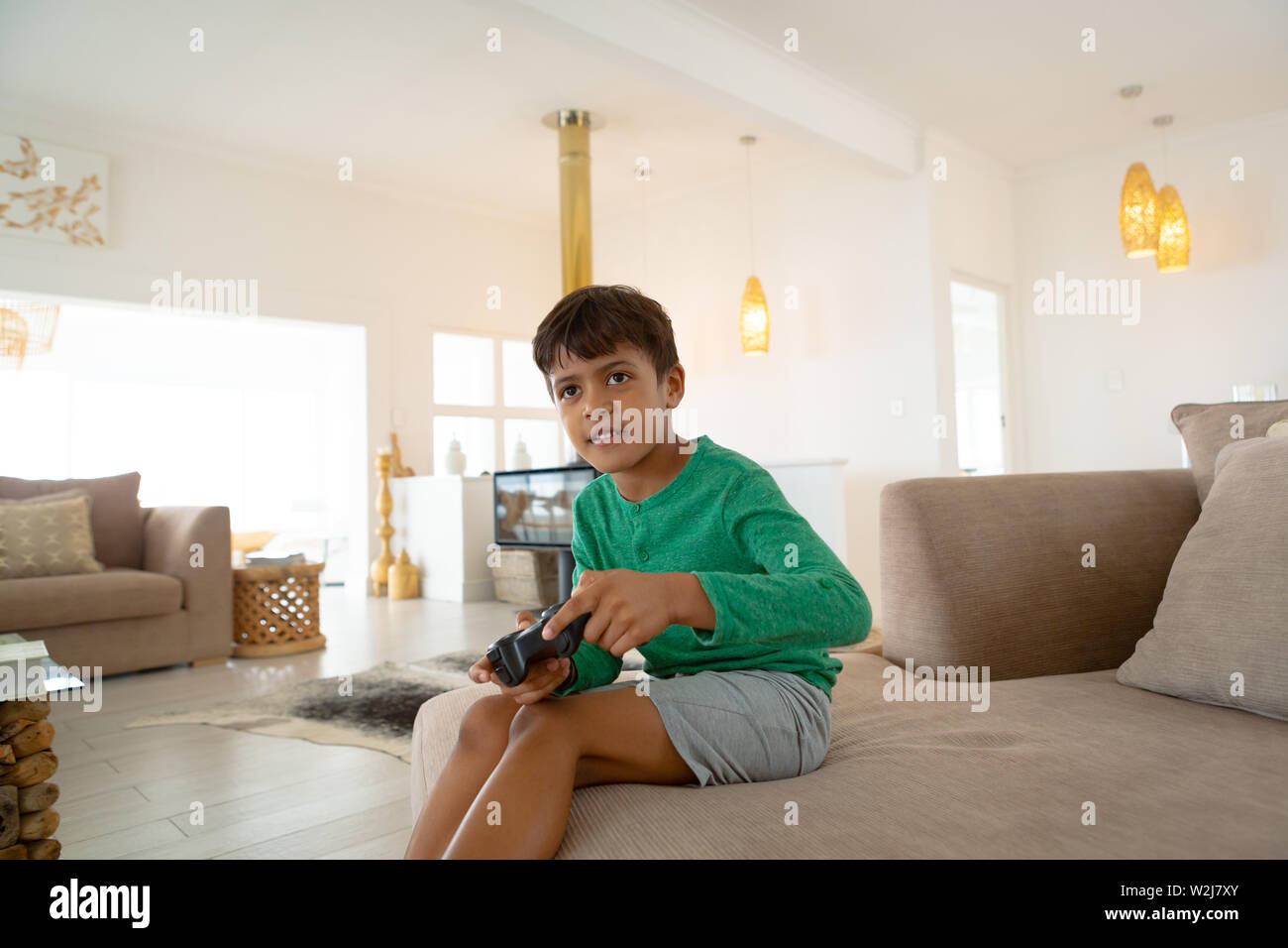 Boy playing video game on sofa in living room at comfortable home Stock Photo