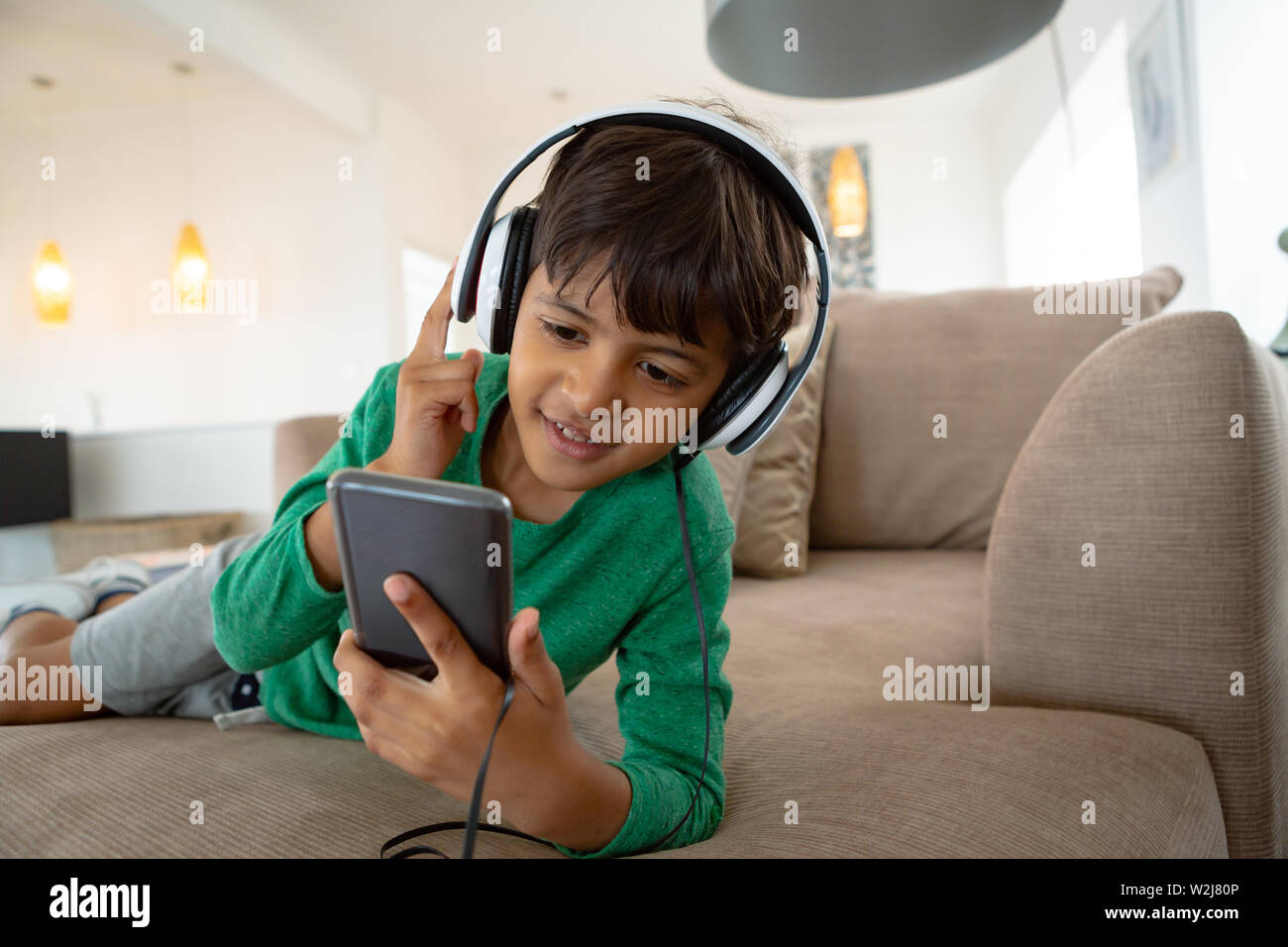 Boy with headset listening music on mobile phone on sofa in a comfortable home Stock Photo