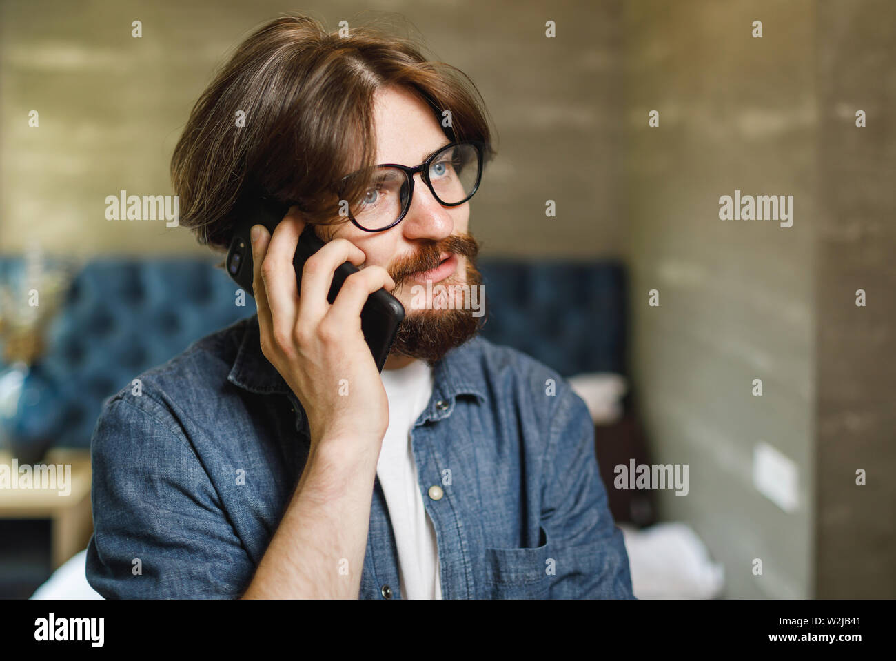 Bearded hipster man wearing glasses speaking on the smartphone at the bedroom Stock Photo