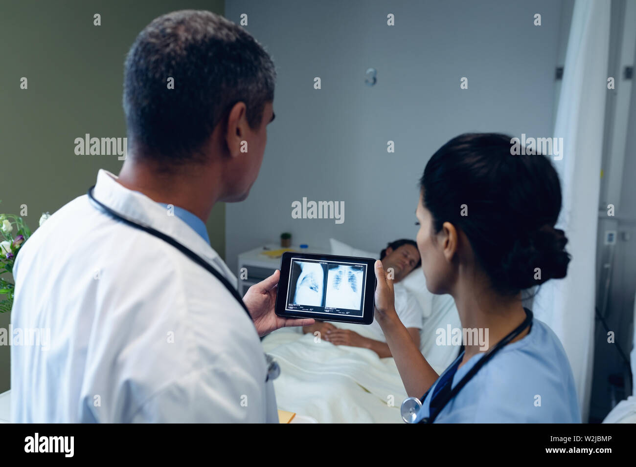 Male and female doctors looking at x-ray report on digital tablet in the ward Stock Photo