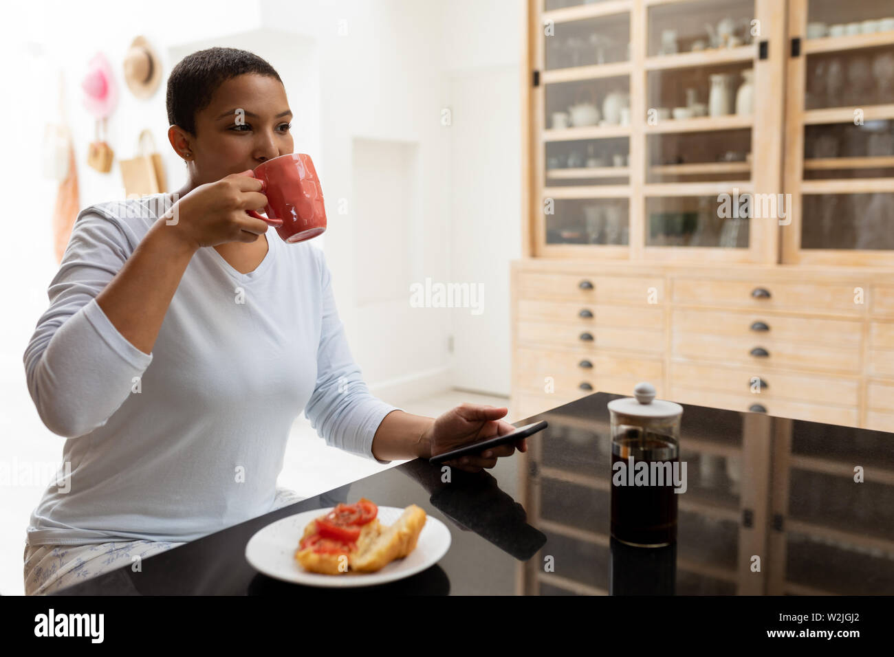 Woman using mobile phone while having coffee on a dining table Stock Photo