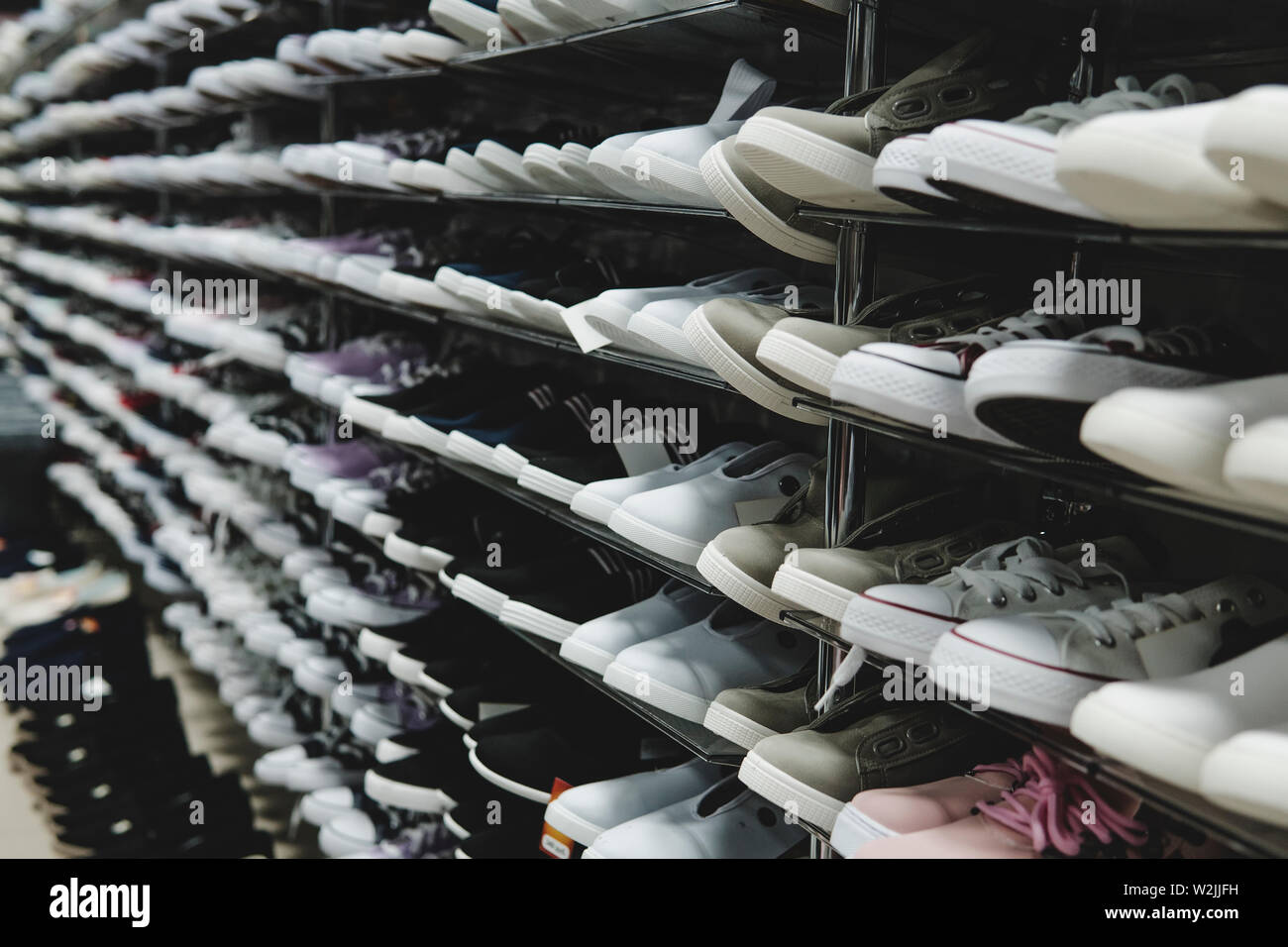 Side view of shoe store shelves with of lots of sneakers on sale. Low-budget comfortable footwear shopping. Unisex stylish teenager shoes. Rows of new Stock Photo