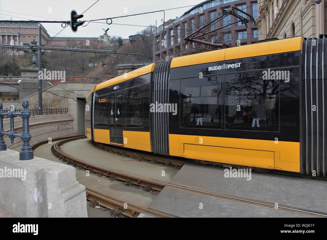 A tram in the Hungarian city of Budapest rounds a bend close to the chain bridge. In the background is the cable car station and Royal Palace Stock Photo