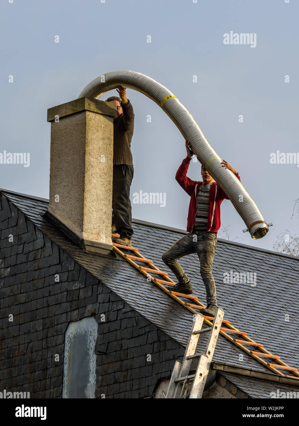 Two men without safety equipment on house roof fitting flue into domestic chimney - France. Stock Photo