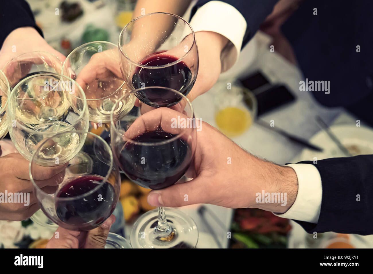 Top-down view of male and female hands with filled glasses of wine above the restaurant tabletop. Drinking toasts and clinking tumblers at a dinner Stock Photo
