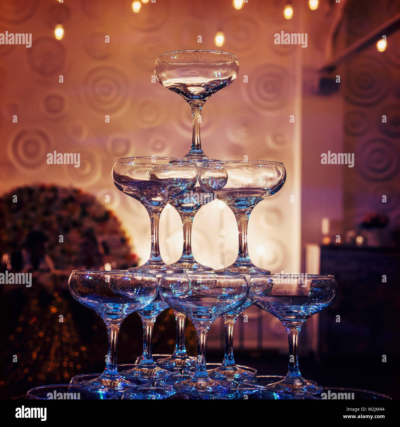 Close up of top tiers of champagne tower at the faint light of a banquet hall. Beautifull built-in set of coupe glasses at a wedding room. Wedding Stock Photo