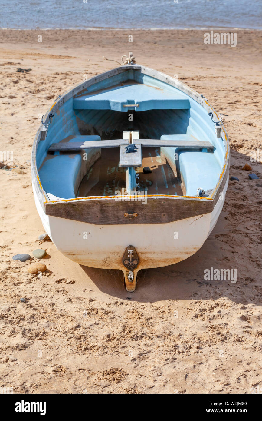 A blue and white rowing boat or skiff on a beach pointing towards the water Stock Photo