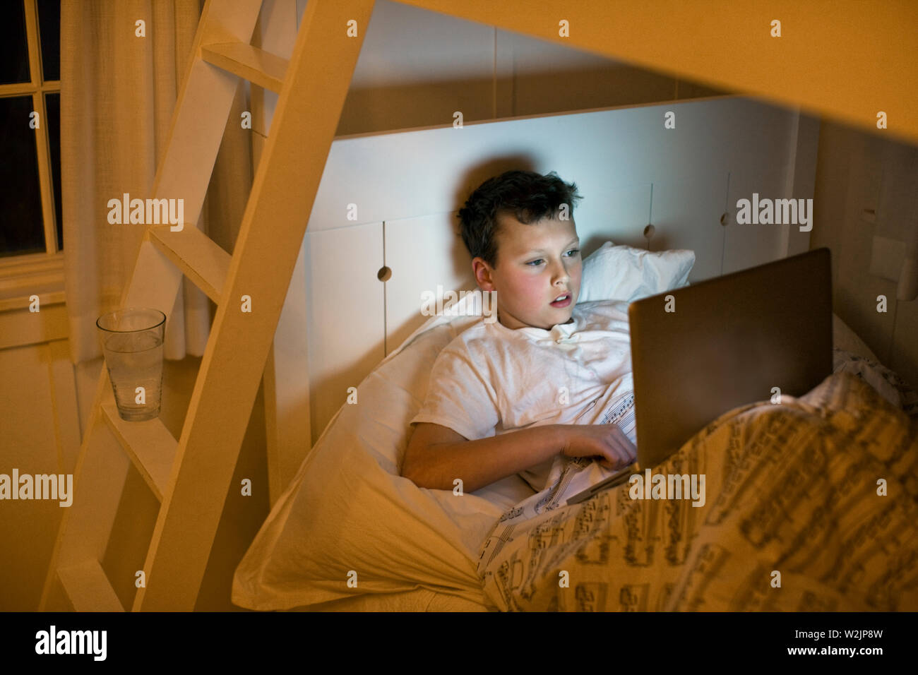 A boy using a laptop in bed at night. Stock Photo