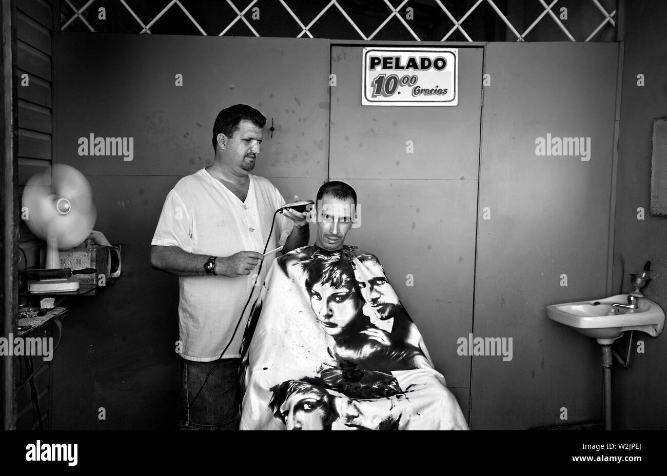 I found this barber working from a shed situated in his front garden. His customer was having a haircut. Stock Photo