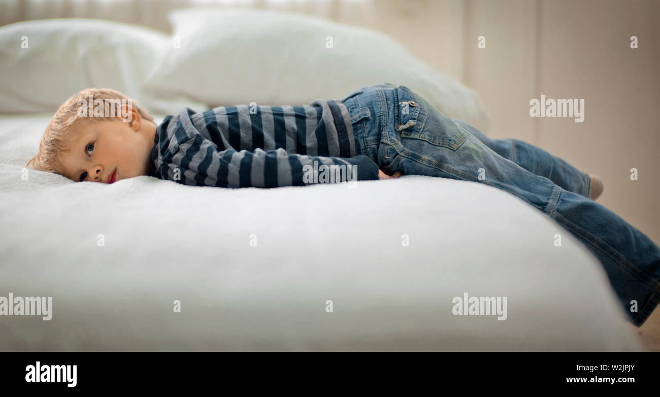 Forlorn looking boy lies on his stomach on a bed. Stock Photo