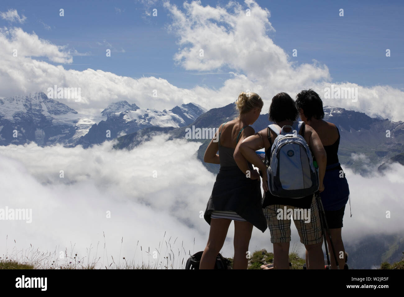 Female hikers enjoying the fine view from Schynige Platte, with a range of snow-capped peaks beyond the cloud-filled Lauterbrunnental, Switzerland Stock Photo