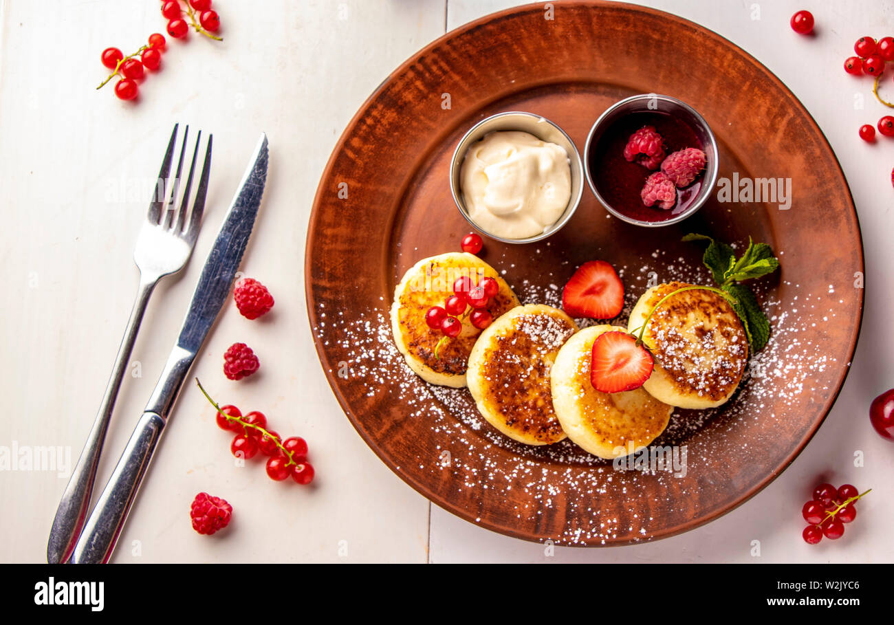 Cottage cheese pancakes, homemade traditional Ukrainian dish syrniki with berry sauce and sour cream on a brown plate on a white background Stock Photo