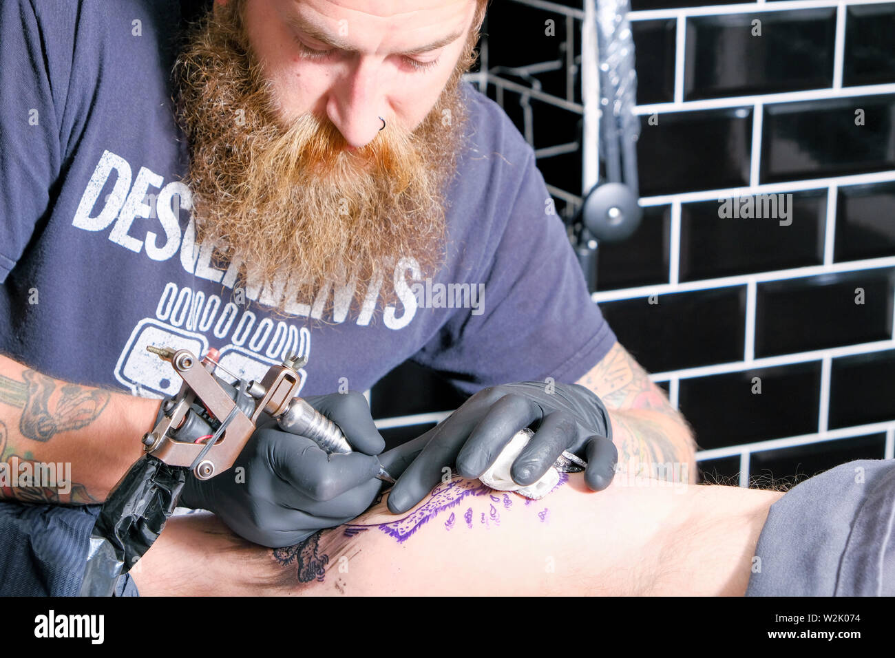 A Tattooist or tattoo artist works on a client creating a tattoo or piece of body art using an electric tattoo machine. Stock Photo
