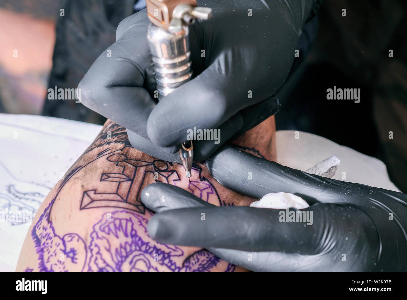 A Tattooist or tattoo artist works on a client creating a tattoo or piece of body art using an electric tattoo machine. Stock Photo