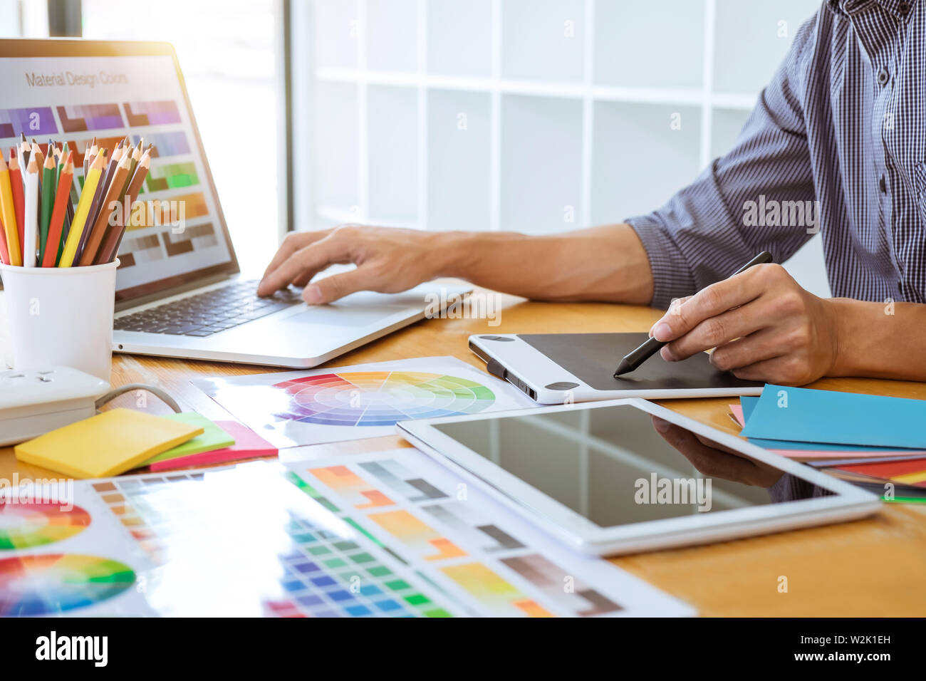 Young creative graphic designer working on project architectural drawing and color swatches, selection coloring on graphic chart with work tools and e Stock Photo