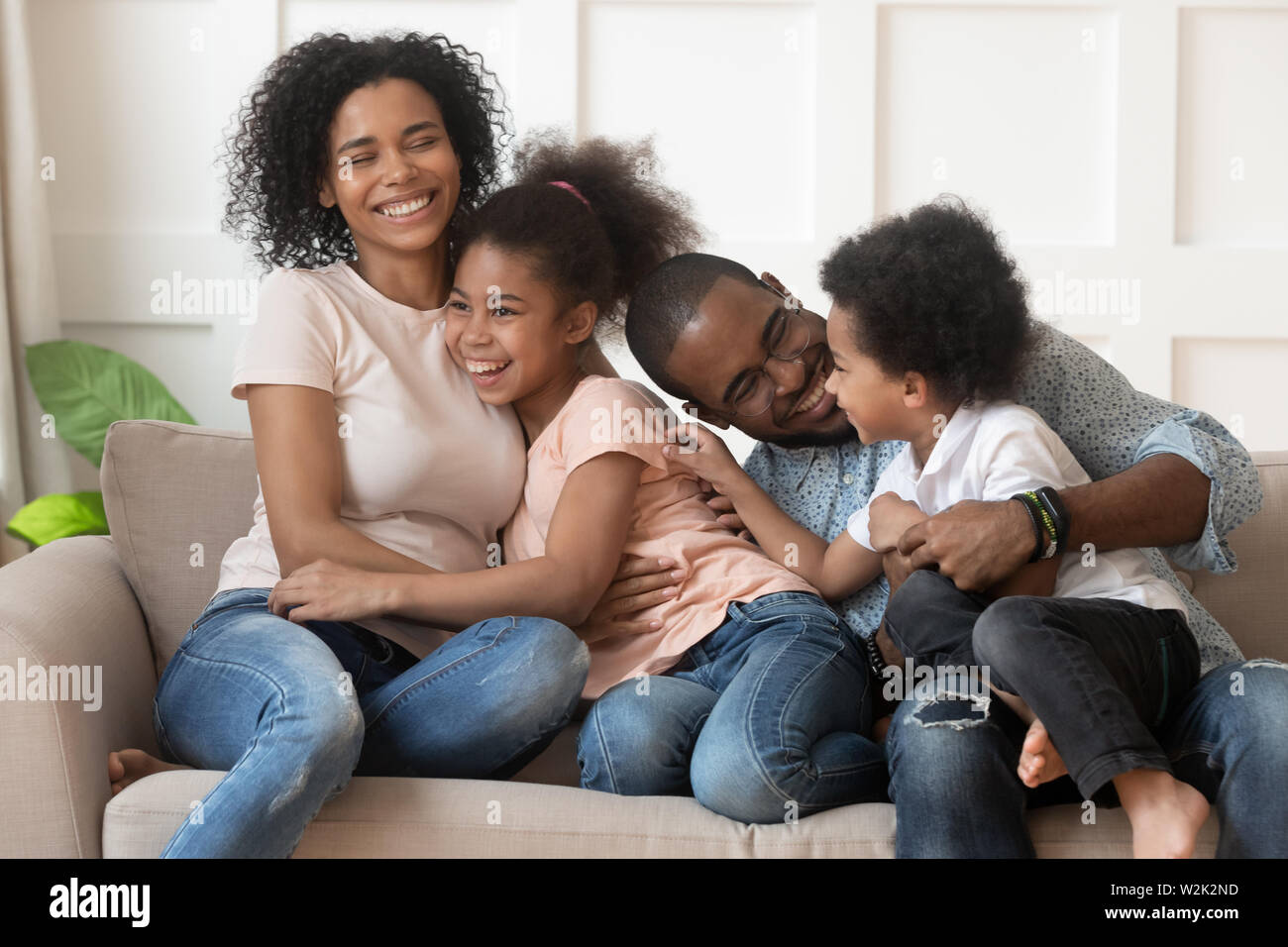 Happy african american family of four laughing bonding on sofa Stock Photo