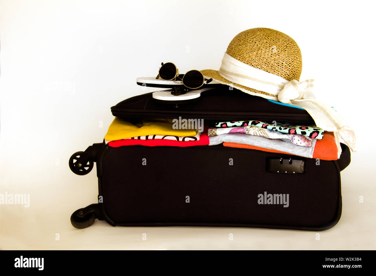 opened suitcase containing clothes with sunglasses and a hat on the top Stock Photo