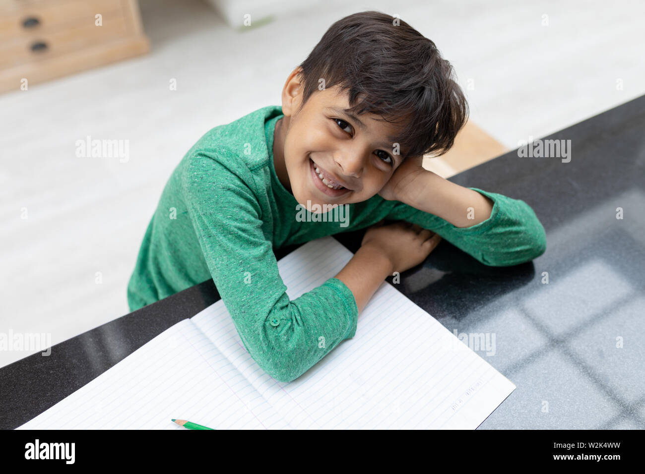 Boy looking at camera while doing his homework on a table Stock Photo