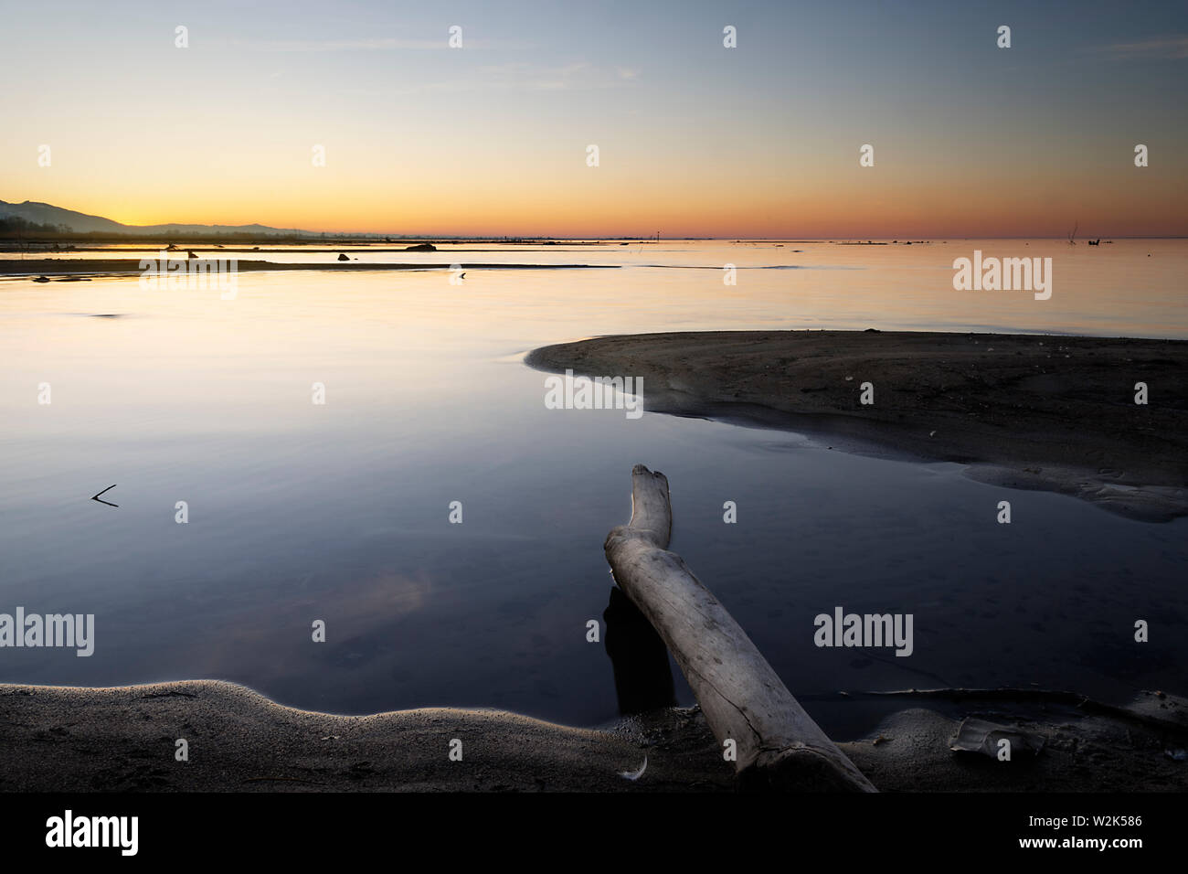 lake at sunset with sand and wood in the foreground Stock Photo