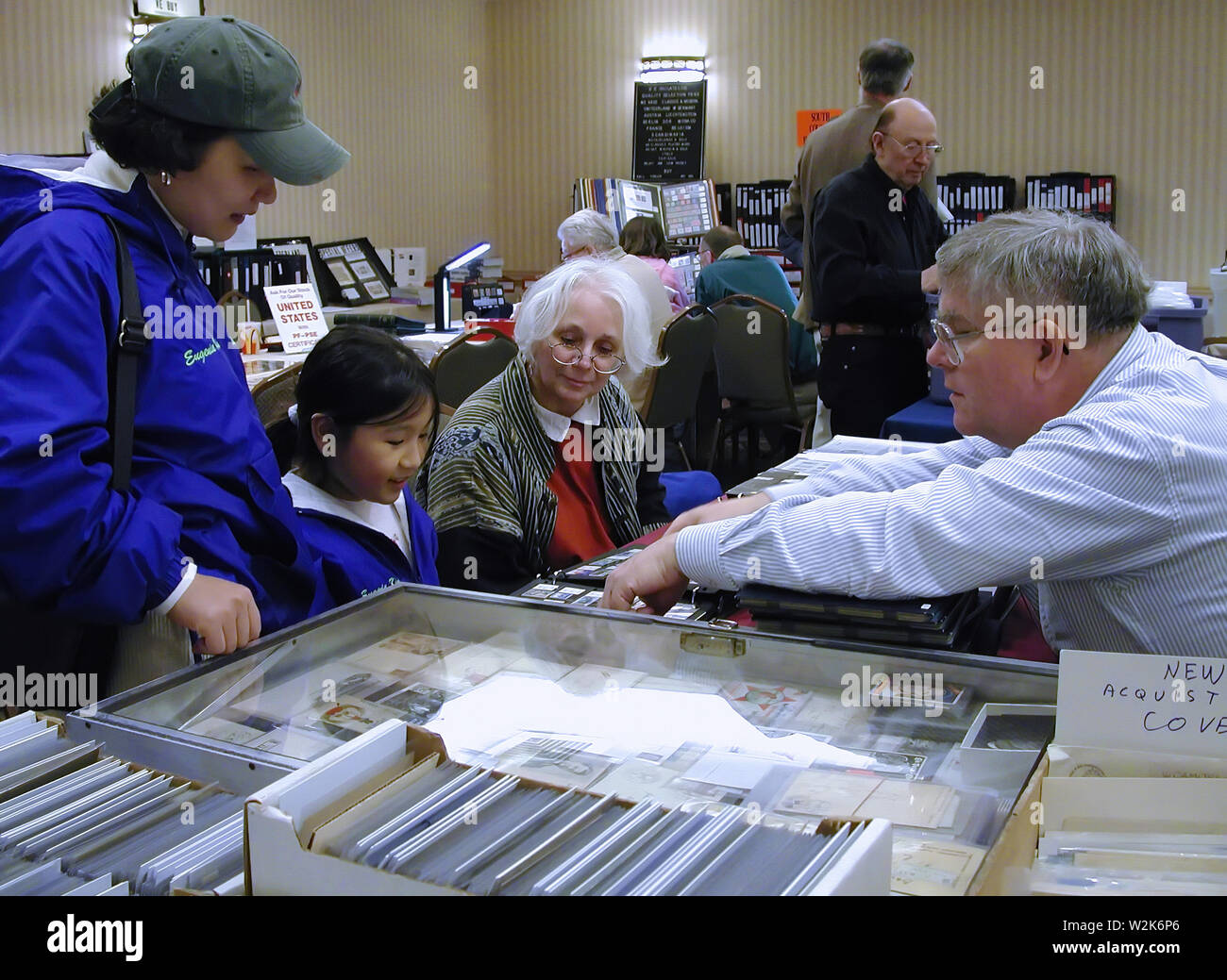 Cromwell, CT USA. Mar 2017. A young Korean American girl is getting some interesting information about stamp collecting from a dealer. Stock Photo