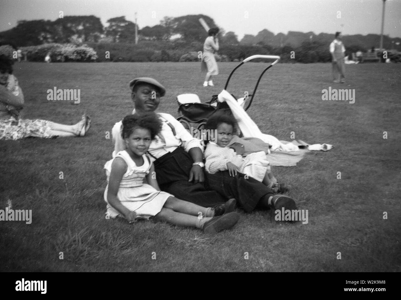 West Indian man relaxing with his children in park Britain 1958 Stock Photo
