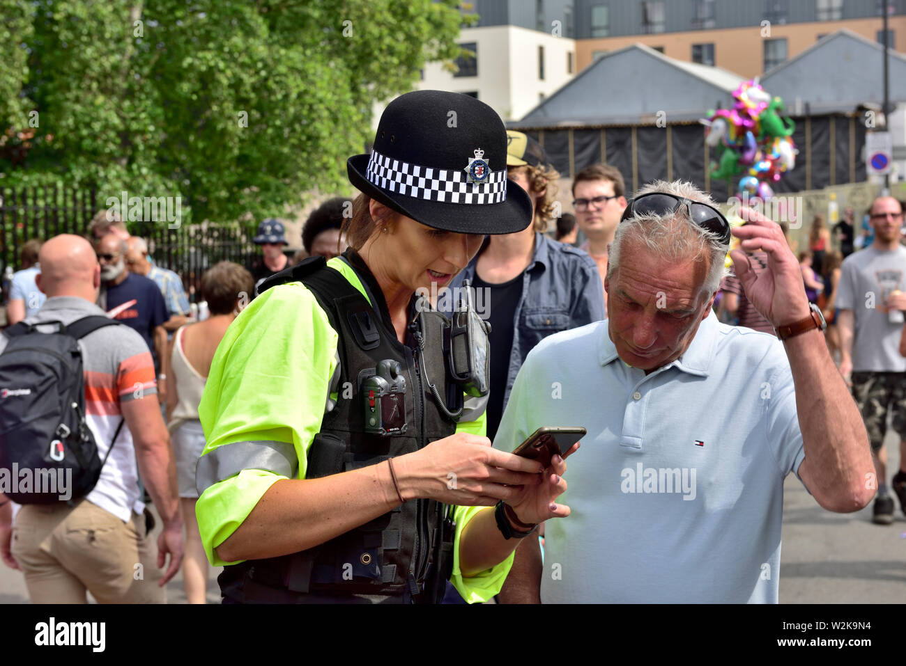 Police woman helping man with map and directions on mobile phone, UK Stock Photo