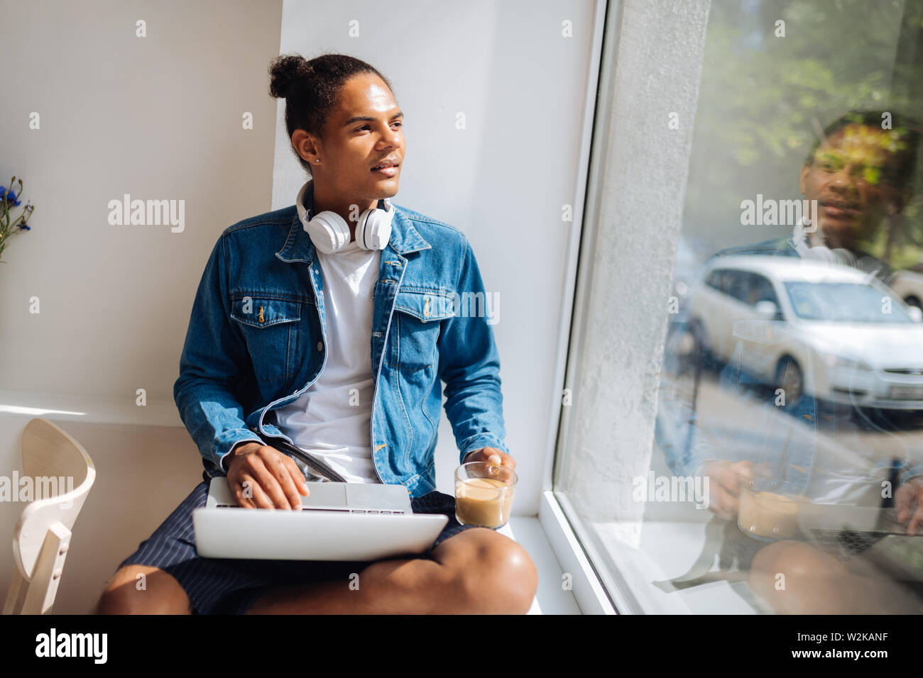 Dreamy mood. Kind male person holding laptop on knees while enjoying view from window Stock Photo