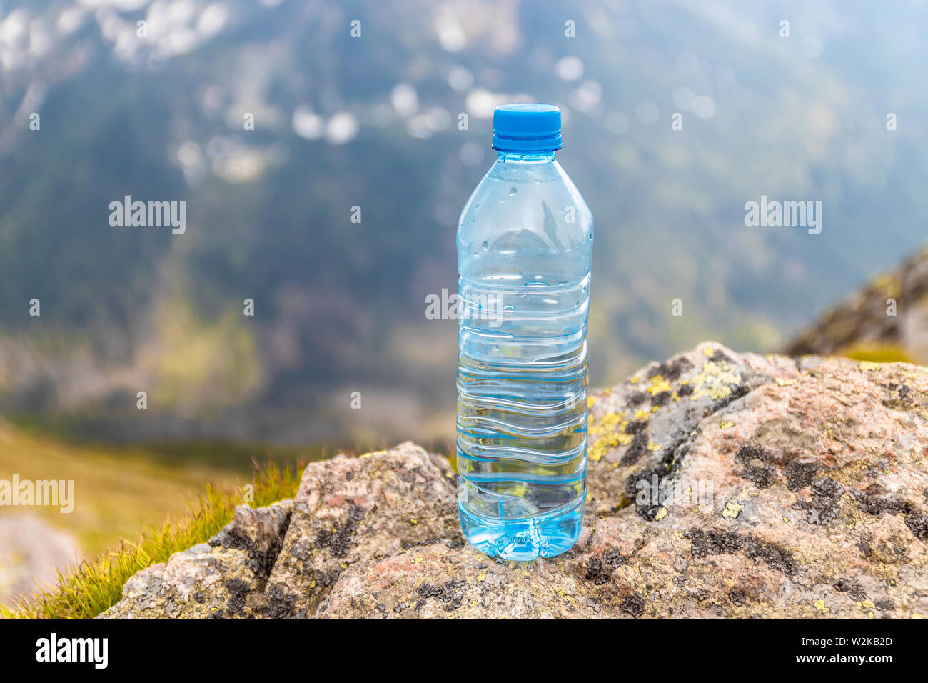 Clear water in a plastic bottle stands on a stone high in the mountains on a sunny day. Stock Photo